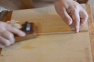 Up-close shot of Eiji planing the wooden chopstick in to shape.