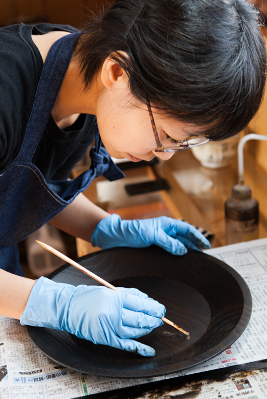 Minako touches up the surface of the large lacquer dish.