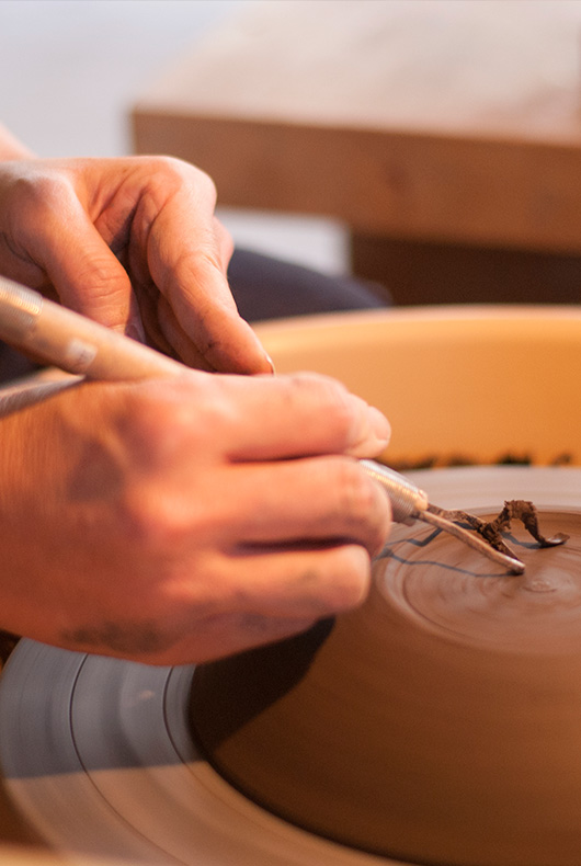 Close up photo of Satoko Suzuki trimming the base of a bowl.