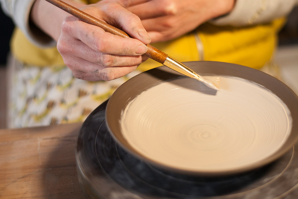 She then applies a slip to the bowl, this will coat the textured body below and add a colour base to the piece.