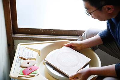 He places a wooden batt on the pottery wheel, making it easy to take the object off the wheel once finished.